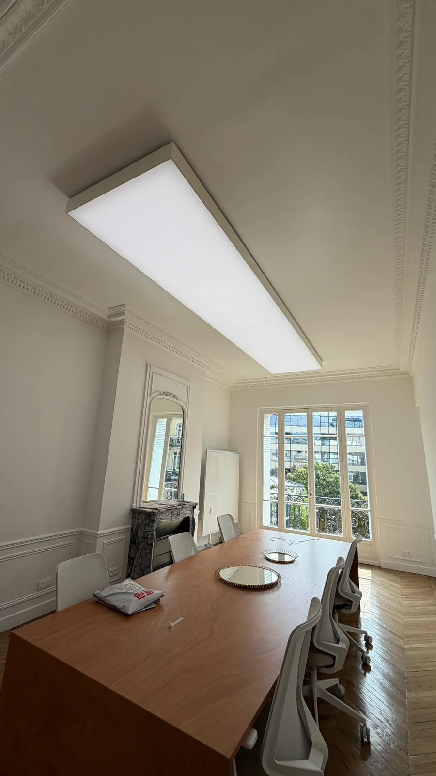 Long surface-mounted luminous ceiling above a Paris office meeting table